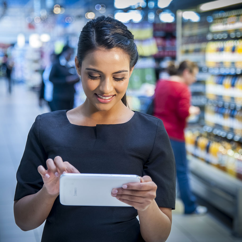 Retail professional using a tablet in a supermarket aisle to analyse shelf layout and product assortment