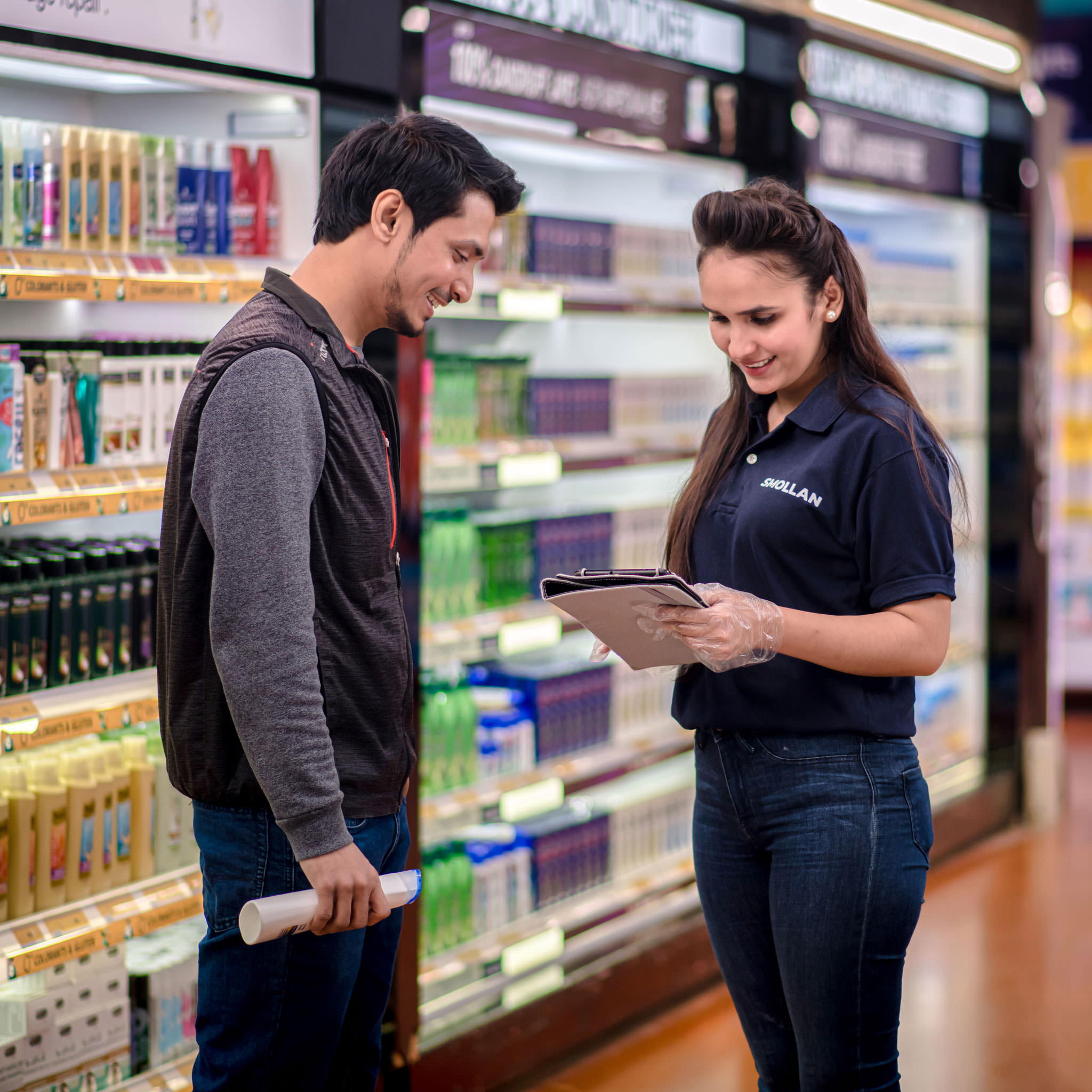Retail representative assisting a shopper in a supermarket aisle using a tablet for product information
